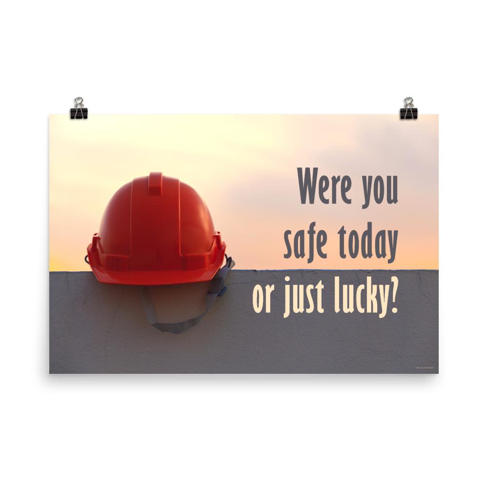 A workplace safety poster showing a red hard hat sitting on a grey wall with a dreamy sunset background and the slogan were you safe today, or just lucky?