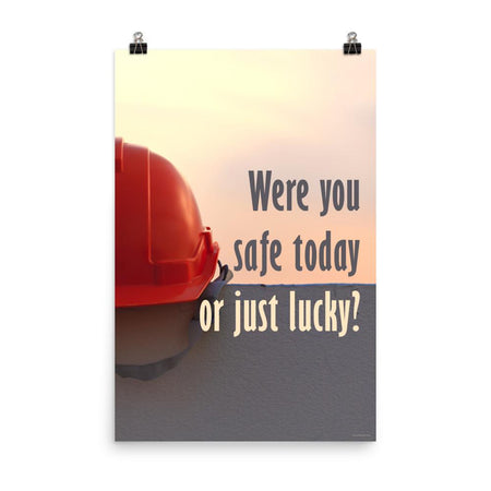 A workplace safety poster showing a red hard hat sitting on a grey wall with a dreamy sunset background and the slogan were you safe today, or just lucky?