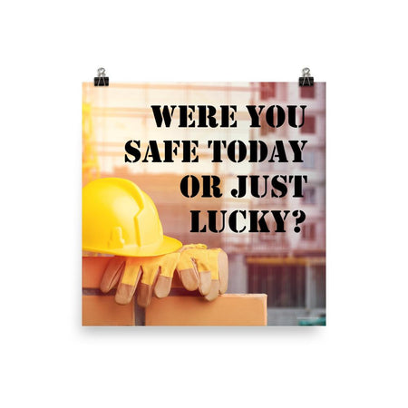 A workplace safety poster showing a yellow hard hat and some gloves sitting on a brick wall on a construction site with the slogan were you safe today, or just lucky written in black stencil font.