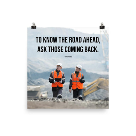 A safety poster showing two workers in reflective vests collaborating on a construction site with the proverb to know the road ahead ask those coming back.