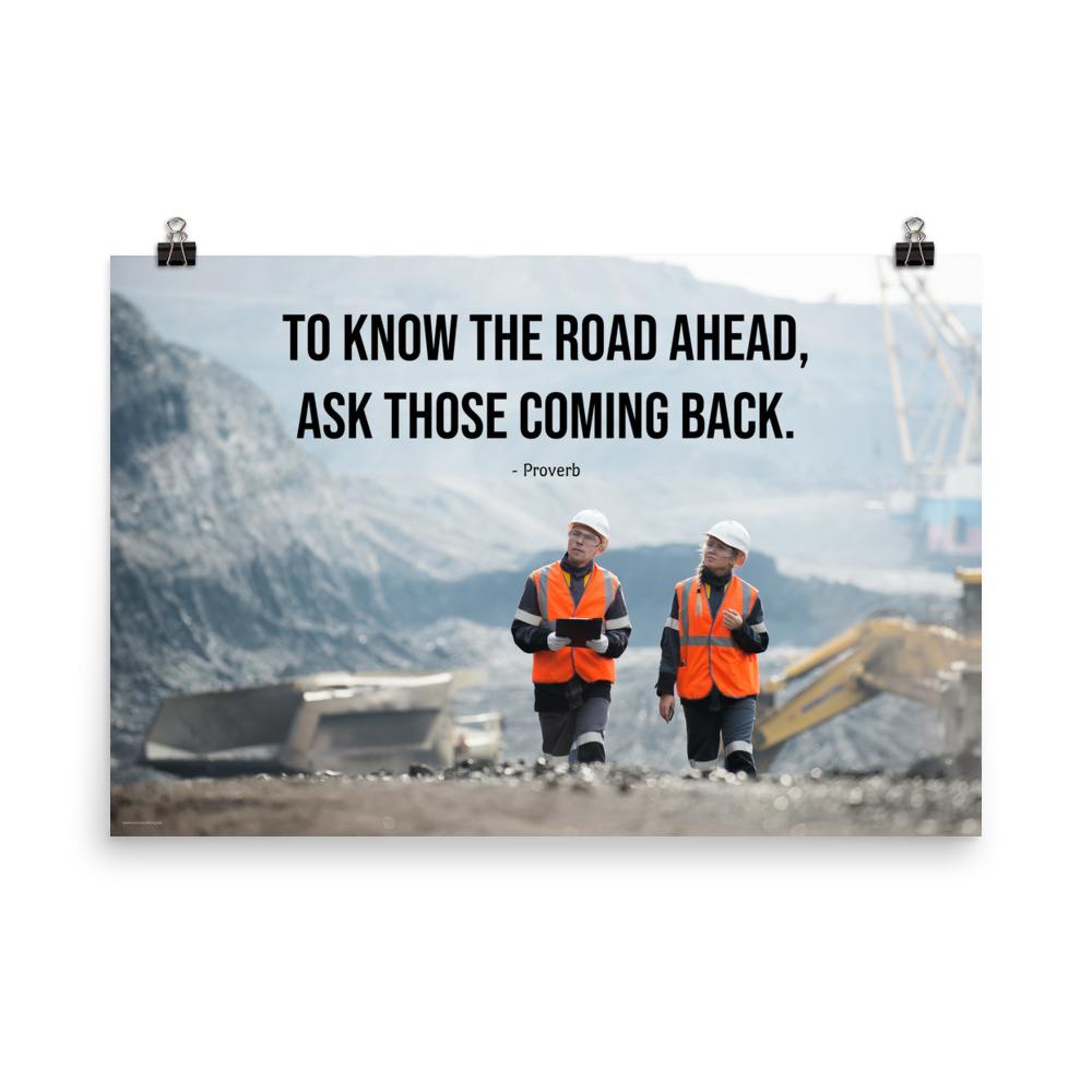 A safety poster showing two workers in reflective vests collaborating on a construction site with the proverb to know the road ahead ask those coming back.