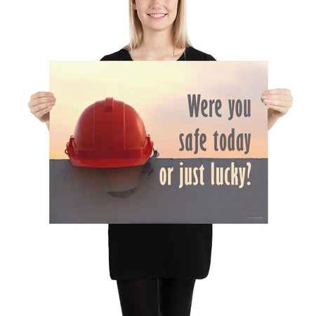 A workplace safety poster showing a red hard hat sitting on a grey wall with a dreamy sunset background and the slogan were you safe today, or just lucky?