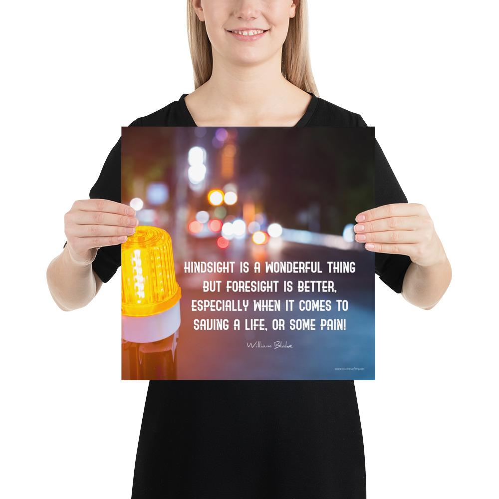 A workplace safety poster depicting a bright orange construction traffic light in the foreground of a blurry nighttime cityscape with a safety quote by William Blake.
