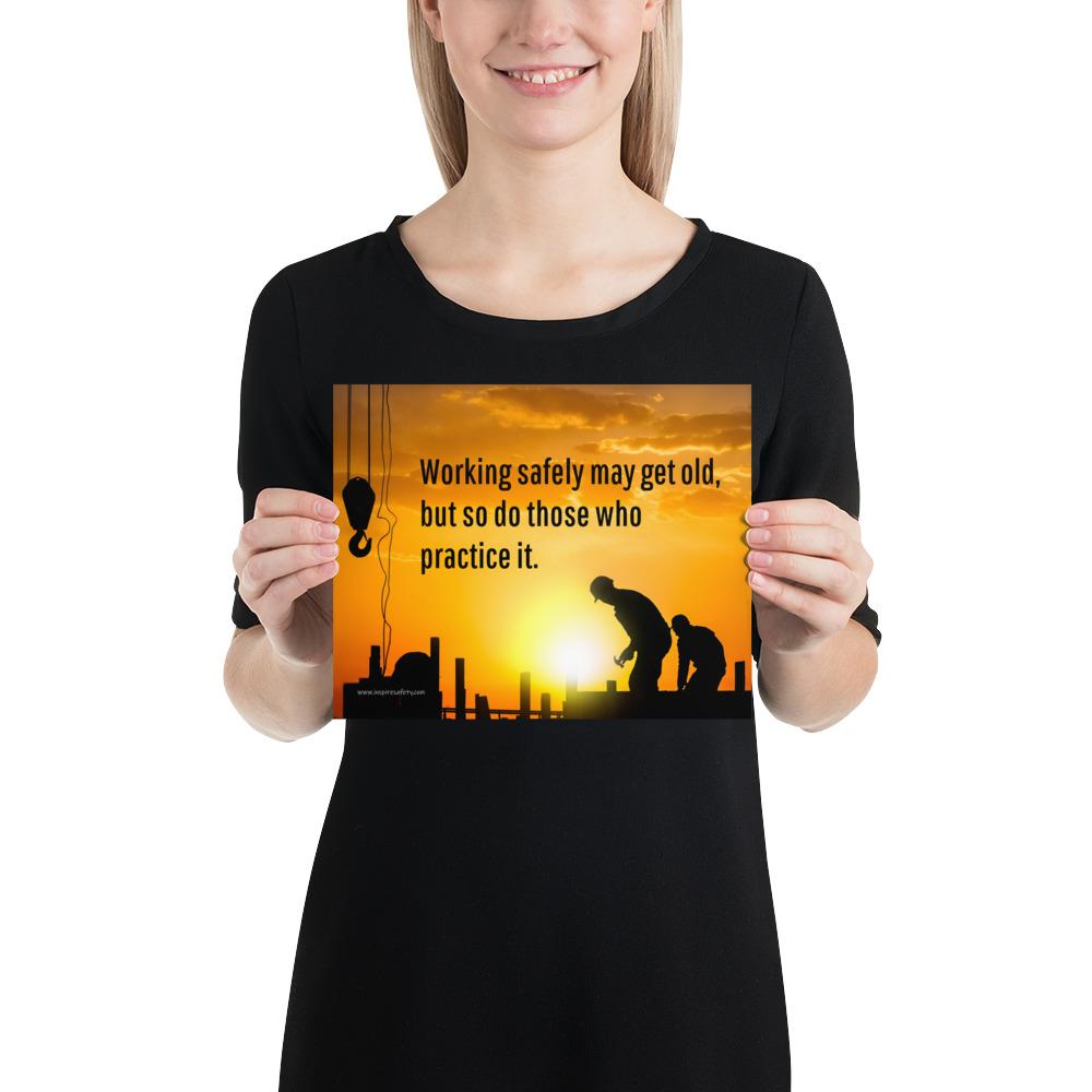 A workplace safety poster showing a construction site and construction workers being silhouetted by a bright and beautiful sunset of different shades of orange with the slogan working safely may get old, but so do those who practice it.