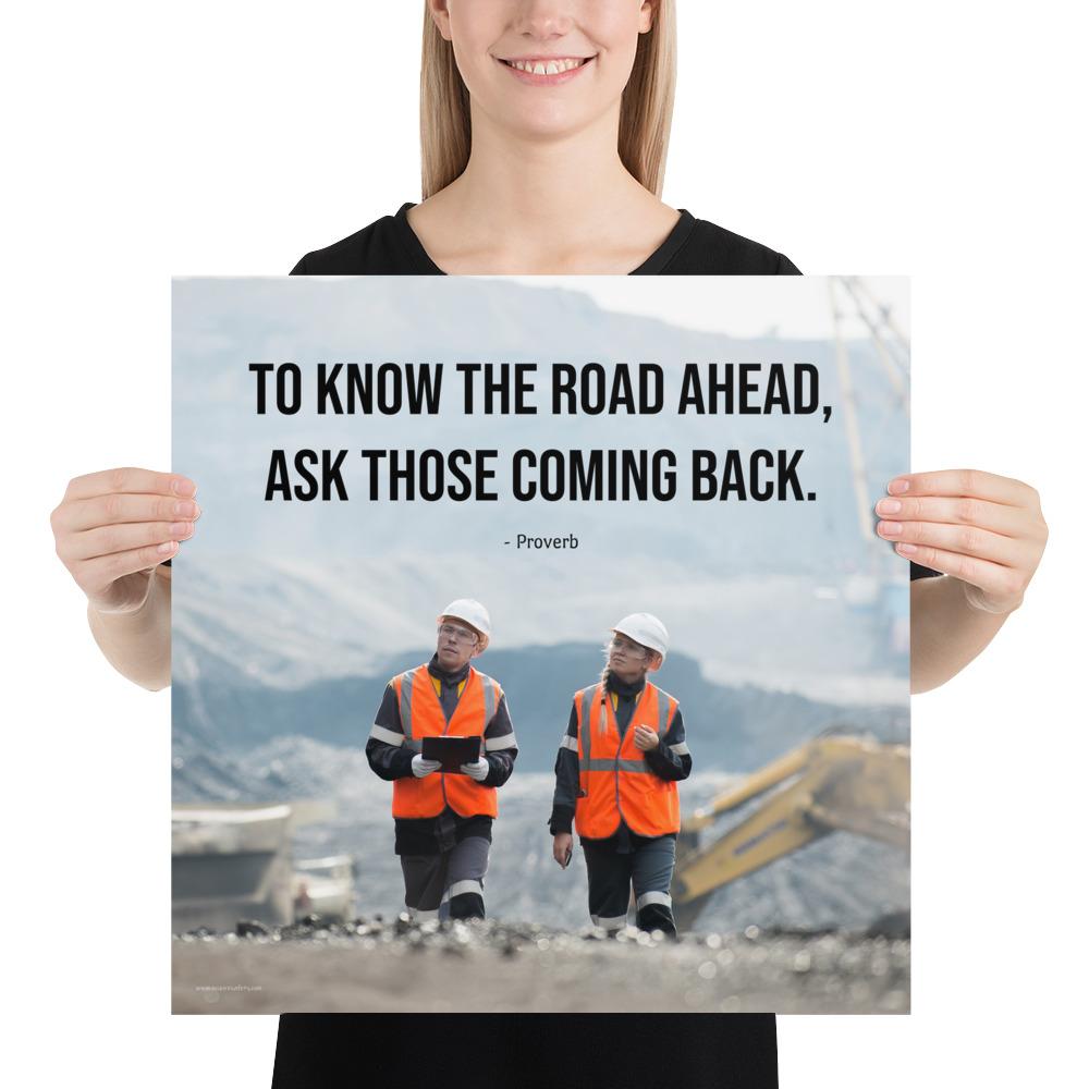 A safety poster showing two workers in reflective vests collaborating on a construction site with the proverb to know the road ahead ask those coming back.