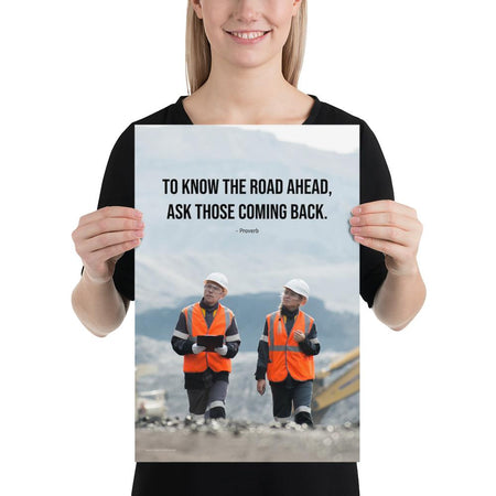 A safety poster showing two workers in reflective vests collaborating on a construction site with the proverb to know the road ahead ask those coming back.