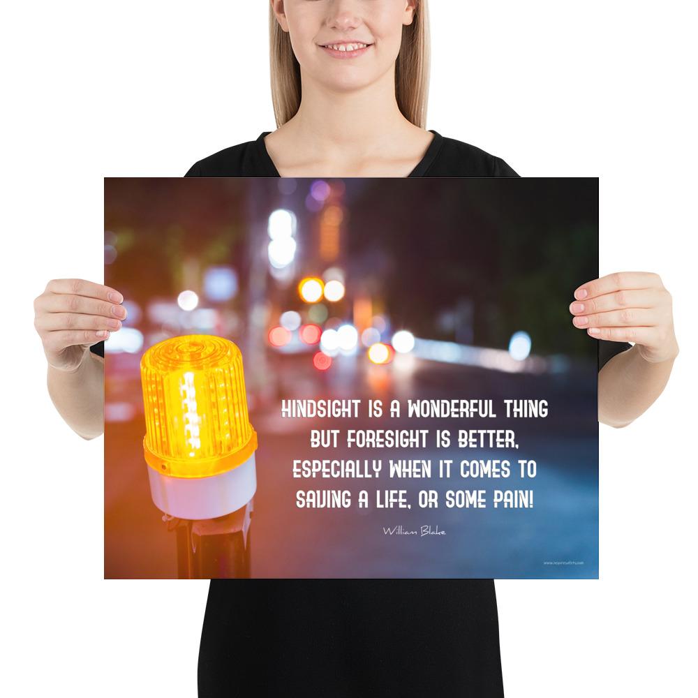 A workplace safety poster depicting a bright orange construction traffic light in the foreground of a blurry nighttime cityscape with a safety quote by William Blake.