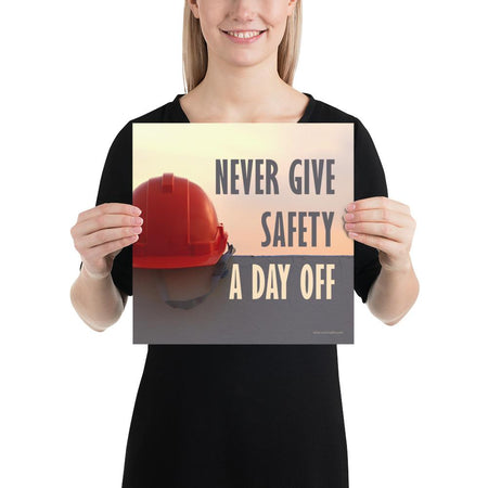 A workplace safety poster depicting a red hard hat sitting on a concrete wall with a dreamy pink sunset in the background with the text never give safety a day off to the right.
