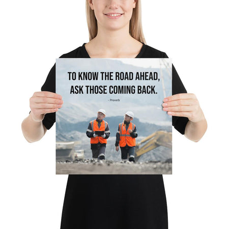 A safety poster showing two workers in reflective vests collaborating on a construction site with the proverb to know the road ahead ask those coming back.