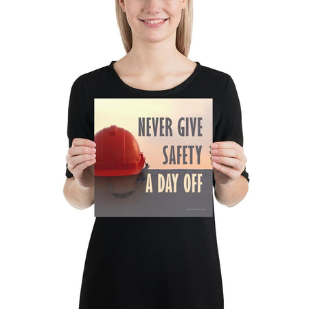 A workplace safety poster depicting a red hard hat sitting on a concrete wall with a dreamy pink sunset in the background with the text never give safety a day off to the right.
