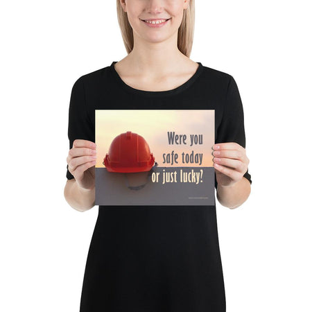 A workplace safety poster showing a red hard hat sitting on a grey wall with a dreamy sunset background and the slogan were you safe today, or just lucky?
