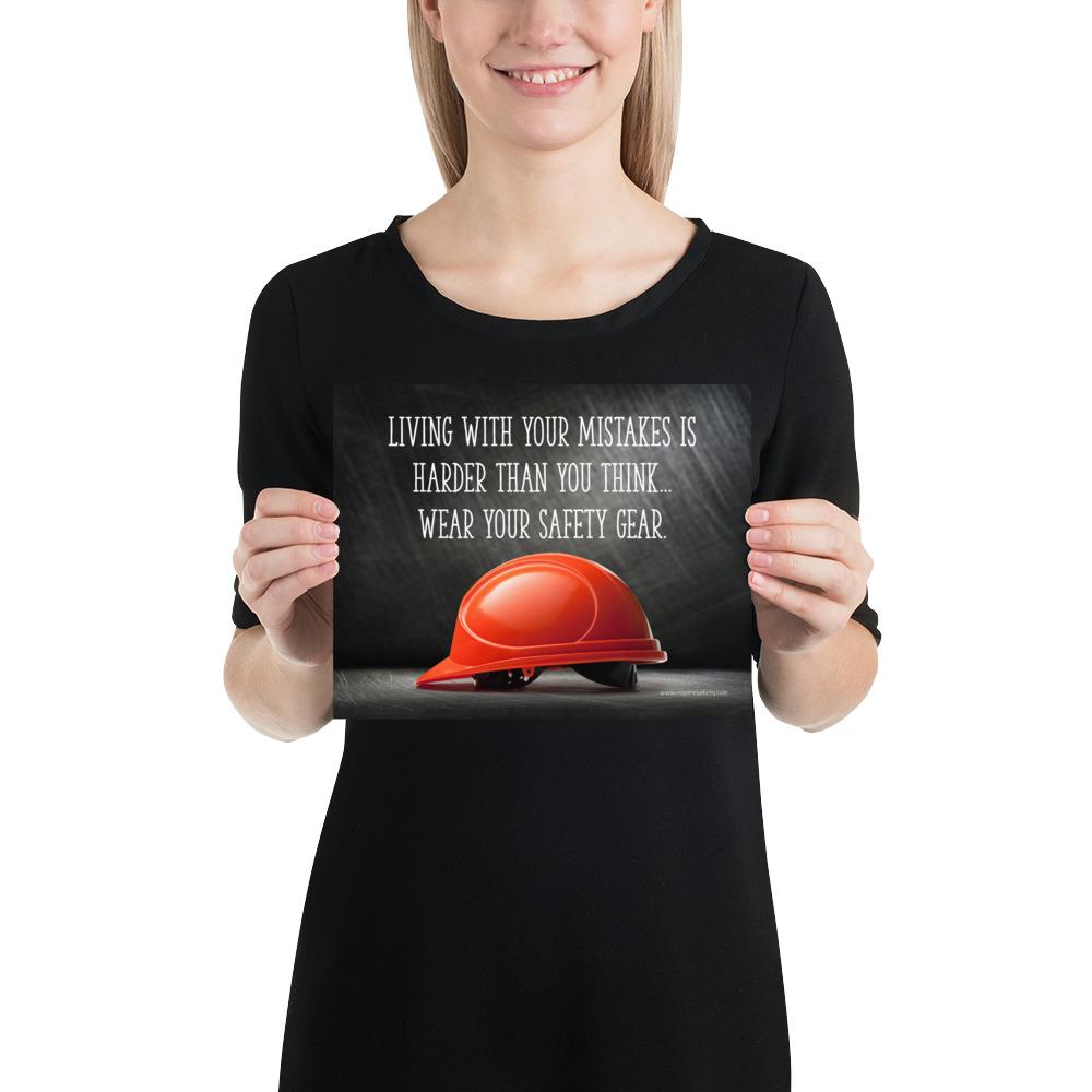 A workplace safety poster showing a bright red hard hat with an ominous black background with the slogan living with your mistakes is harder than you think, wear your safety gear.