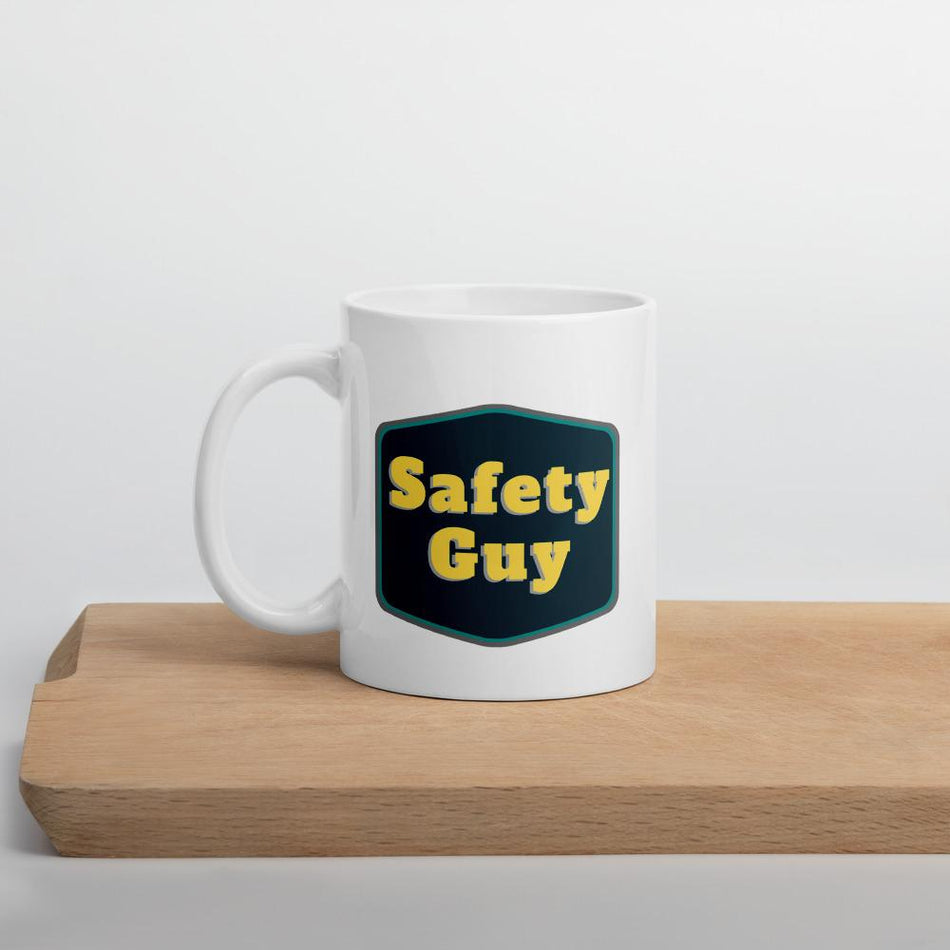 White ceramic mug with a navy emblem encasing bold yellow text that says "Safety Guy."