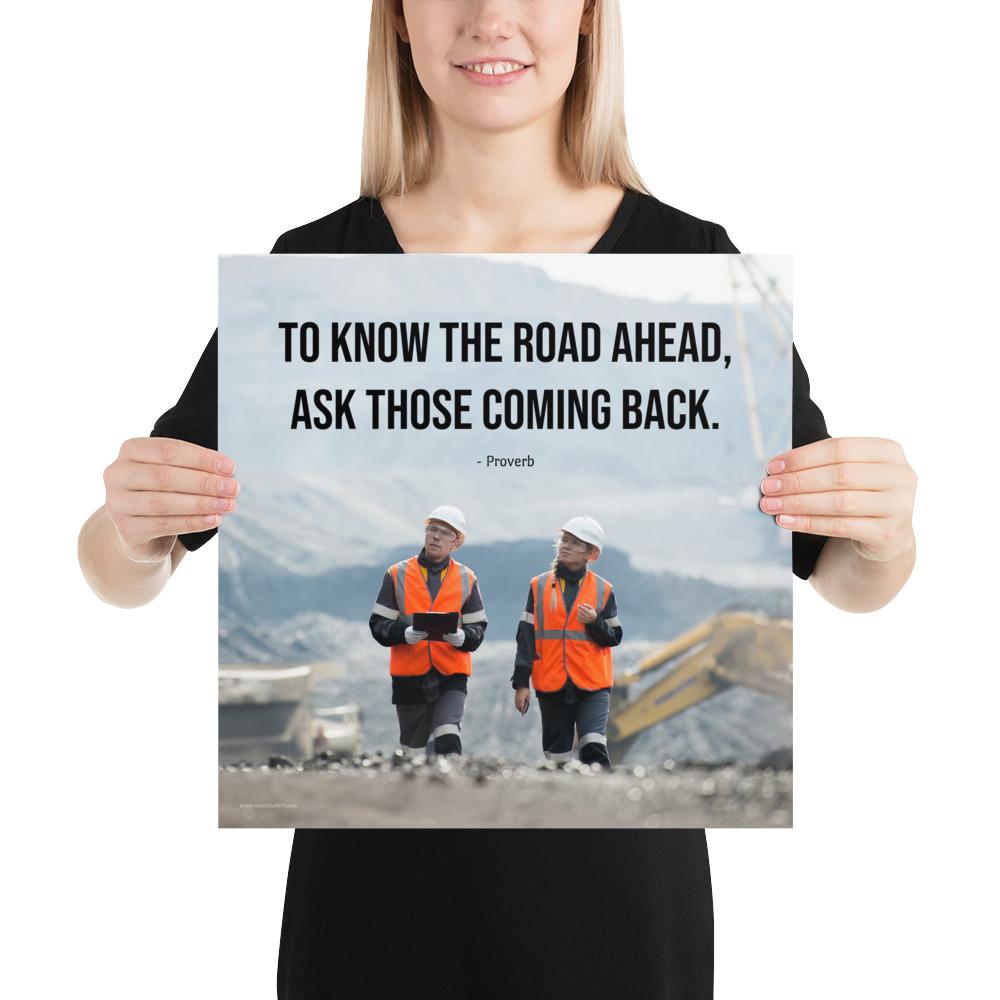 A safety poster showing two workers in reflective vests collaborating on a construction site with the proverb to know the road ahead ask those coming back.