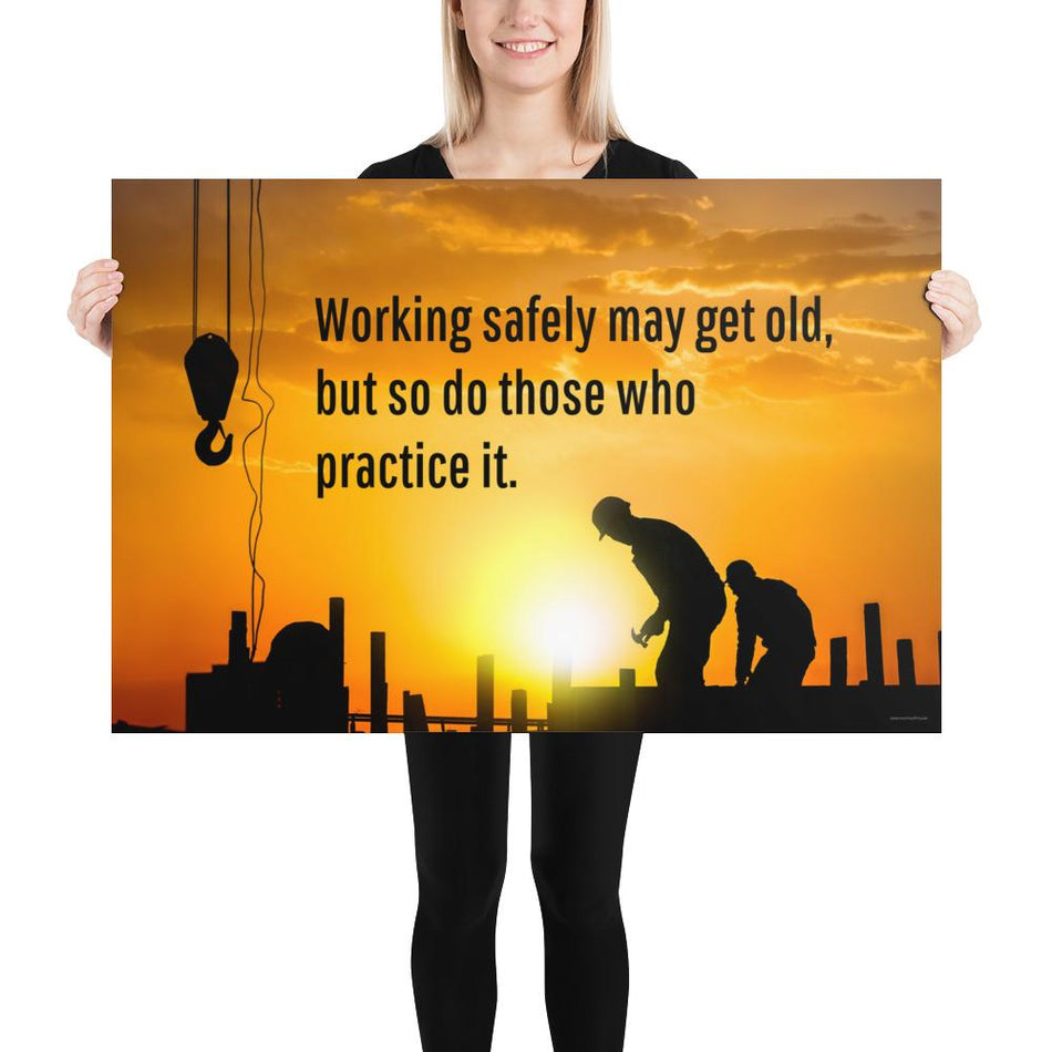 A workplace safety poster showing a construction site and construction workers being silhouetted by a bright and beautiful sunset of different shades of orange with the slogan working safely may get old, but so do those who practice it.