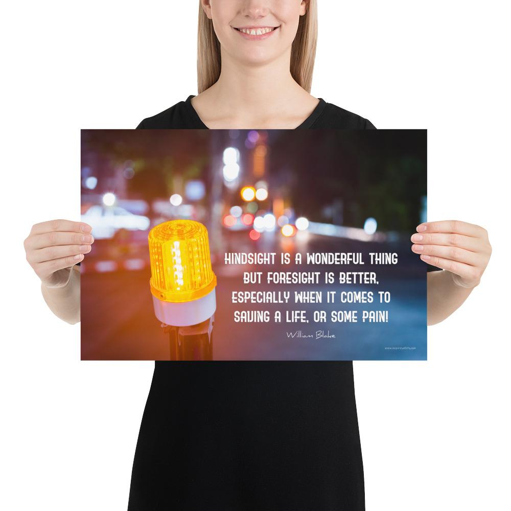 A workplace safety poster depicting a bright orange construction traffic light in the foreground of a blurry nighttime cityscape with a safety quote by William Blake.