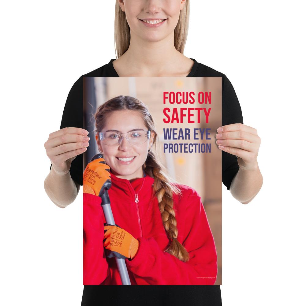 An eye safety poster of a young woman wearing safety glasses and orange gloves smiling as she works in a warehouse with a safety slogan in the top right corner.