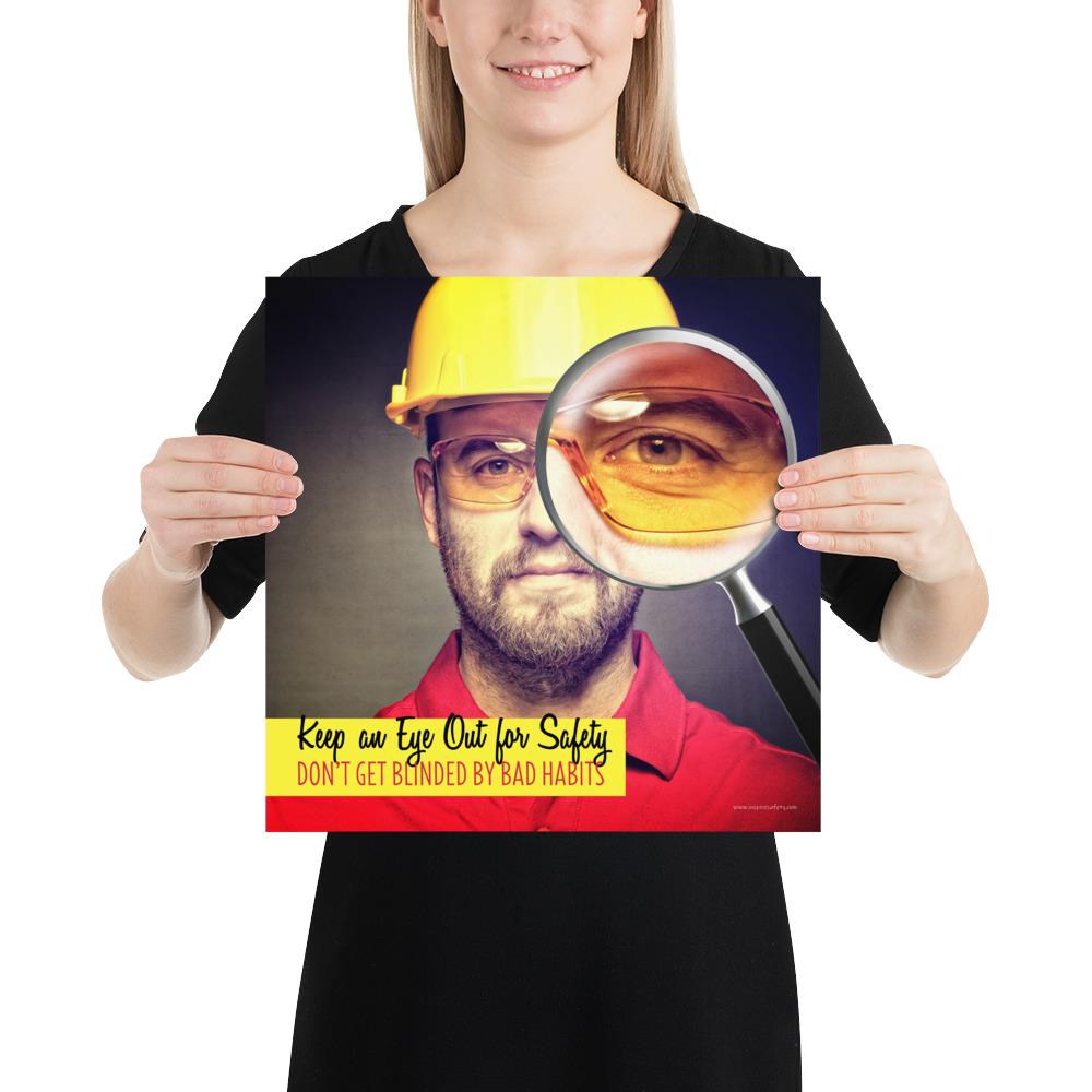 A workplace safety poster showing a portrait of a man wearing a hardhat and safety glasses with a magnifying glass magnifying one eye with the slogan, keep an eye out for safety, don't get blinded by bad habits.
