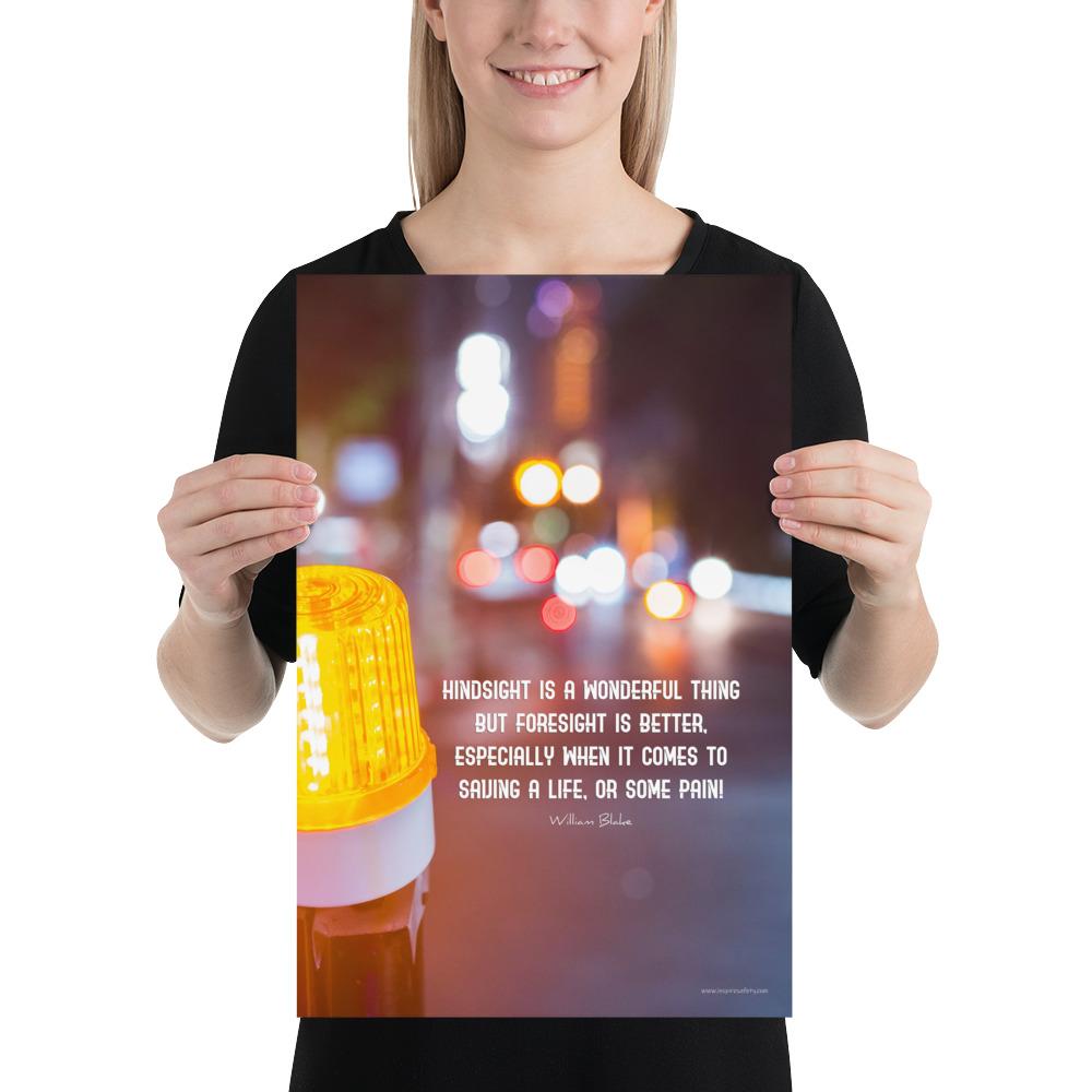 A workplace safety poster depicting a bright orange construction traffic light in the foreground of a blurry nighttime cityscape with a safety quote by William Blake.