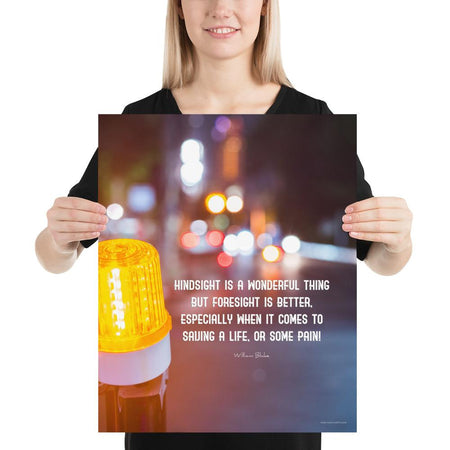 A workplace safety poster depicting a bright orange construction traffic light in the foreground of a blurry nighttime cityscape with a safety quote by William Blake.