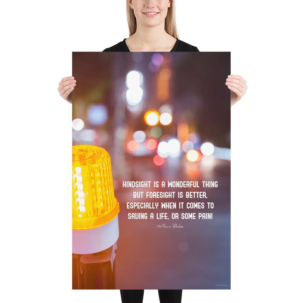 A workplace safety poster depicting a bright orange construction traffic light in the foreground of a blurry nighttime cityscape with a safety quote by William Blake.