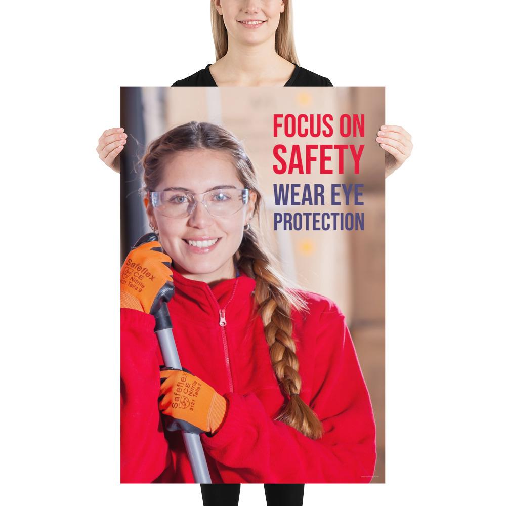 An eye safety poster of a young woman wearing safety glasses and orange gloves smiling as she works in a warehouse with a safety slogan in the top right corner.