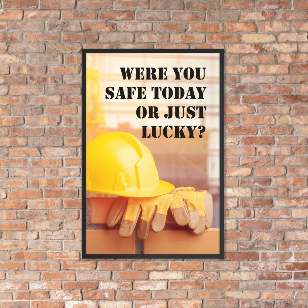 A workplace safety poster showing a yellow hard hat and some gloves sitting on a brick wall on a construction site with the slogan were you safe today, or just lucky written in black stencil font.