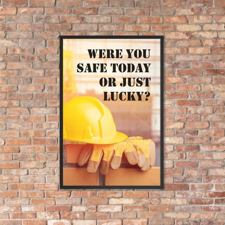 A workplace safety poster showing a yellow hard hat and some gloves sitting on a brick wall on a construction site with the slogan were you safe today, or just lucky written in black stencil font.