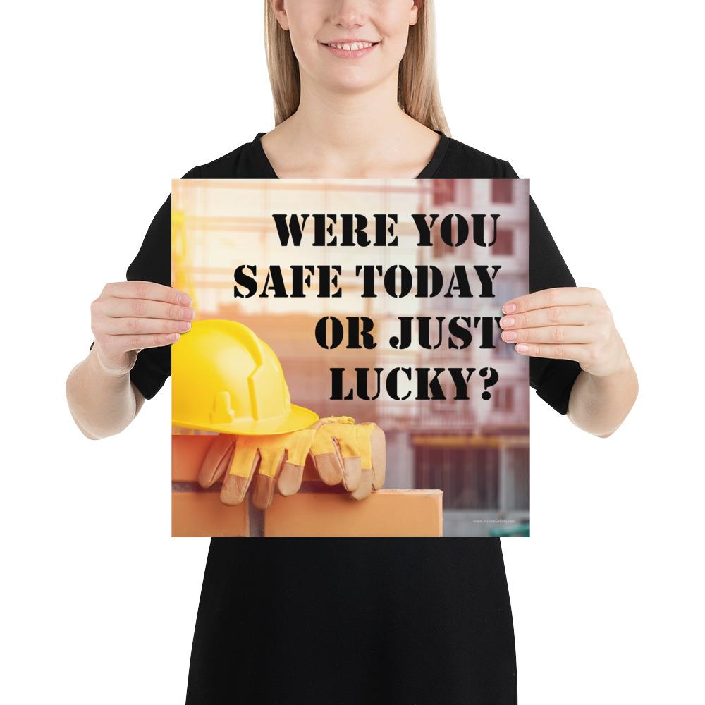 A workplace safety poster showing a yellow hard hat and some gloves sitting on a brick wall on a construction site with the slogan were you safe today, or just lucky written in black stencil font.