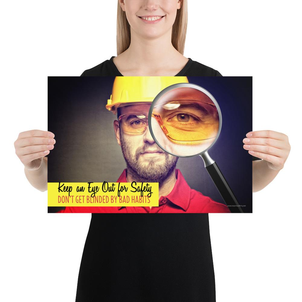 A workplace safety poster showing a portrait of a man wearing a hardhat and safety glasses with a magnifying glass magnifying one eye with the slogan, keep an eye out for safety, don't get blinded by bad habits.