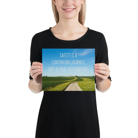 A workplace safety poster depicting a beautiful sunny day with a bright blue sky and a lush green field being cut down the middle by a dirt road leading off into the countryside with the text safety is a continuing journey, not a final destination.