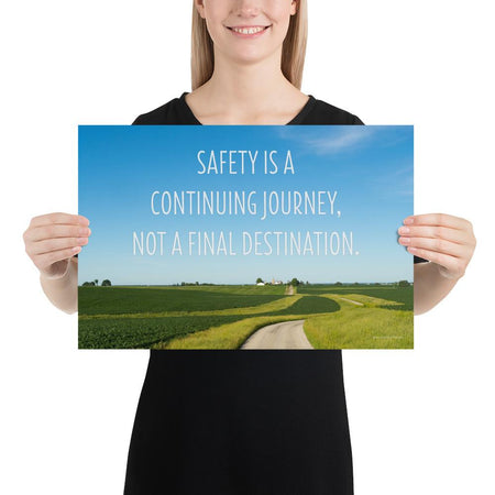A workplace safety poster depicting a beautiful sunny day with a bright blue sky and a lush green field being cut down the middle by a dirt road leading off into the countryside with the text safety is a continuing journey, not a final destination.