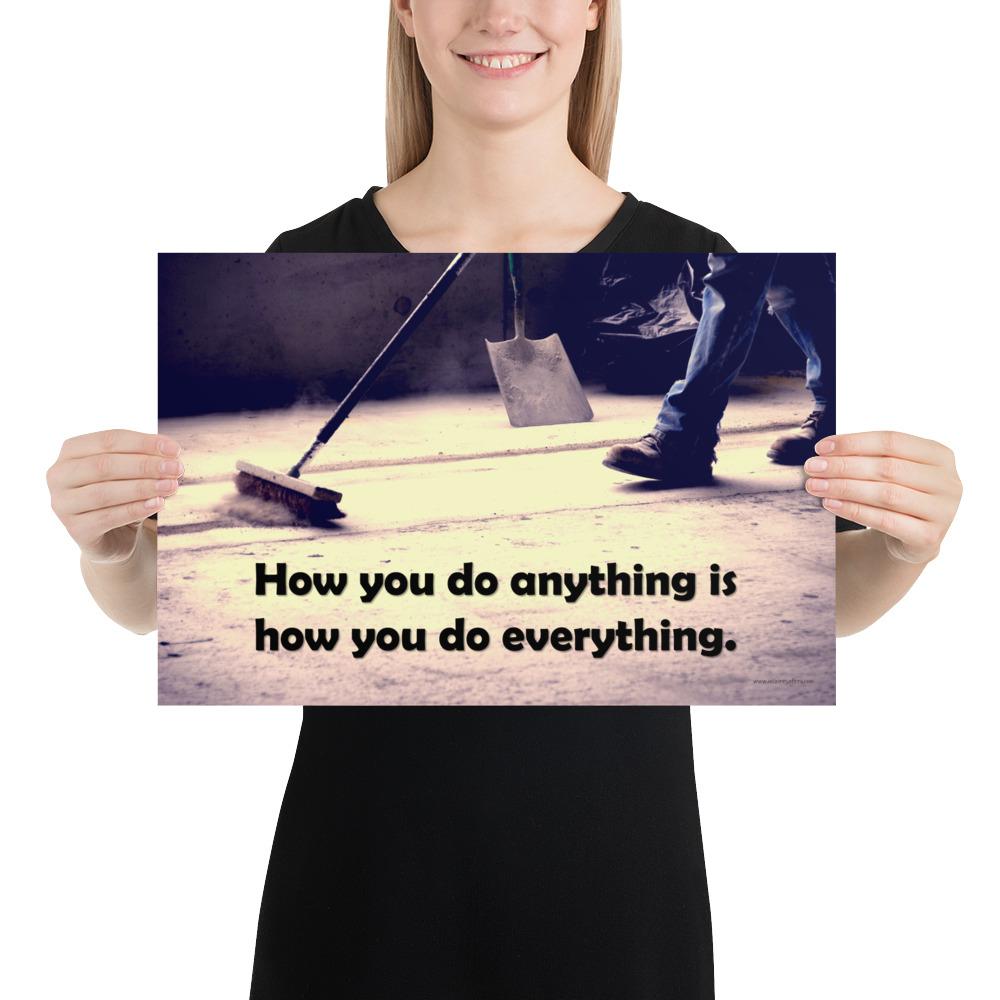Safety poster showing a closeup of the ground where a warehouse or construction worker is sweeping the workshop floor and an encouraging safety slogan written in bold text.