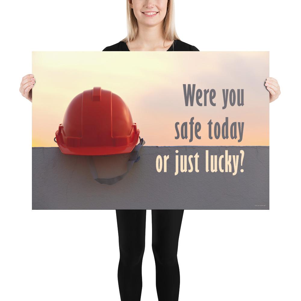 A workplace safety poster showing a red hard hat sitting on a grey wall with a dreamy sunset background and the slogan were you safe today, or just lucky?