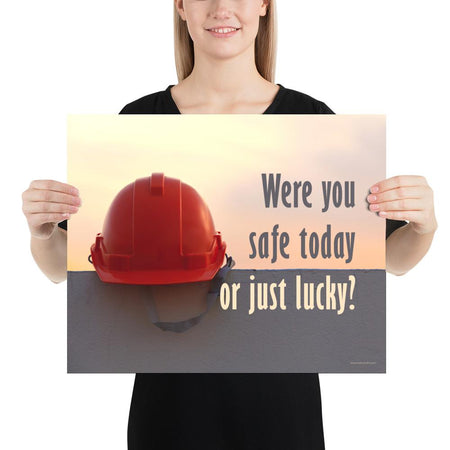 A workplace safety poster showing a red hard hat sitting on a grey wall with a dreamy sunset background and the slogan were you safe today, or just lucky?