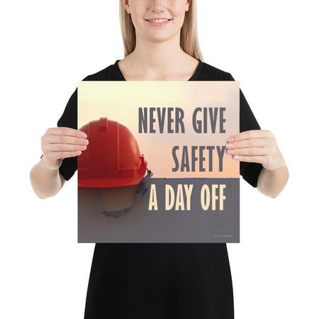 A workplace safety poster depicting a red hard hat sitting on a concrete wall with a dreamy pink sunset in the background with the text never give safety a day off to the right.