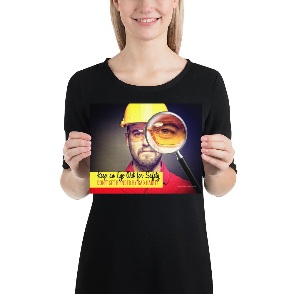A workplace safety poster showing a portrait of a man wearing a hardhat and safety glasses with a magnifying glass magnifying one eye with the slogan, keep an eye out for safety, don't get blinded by bad habits.