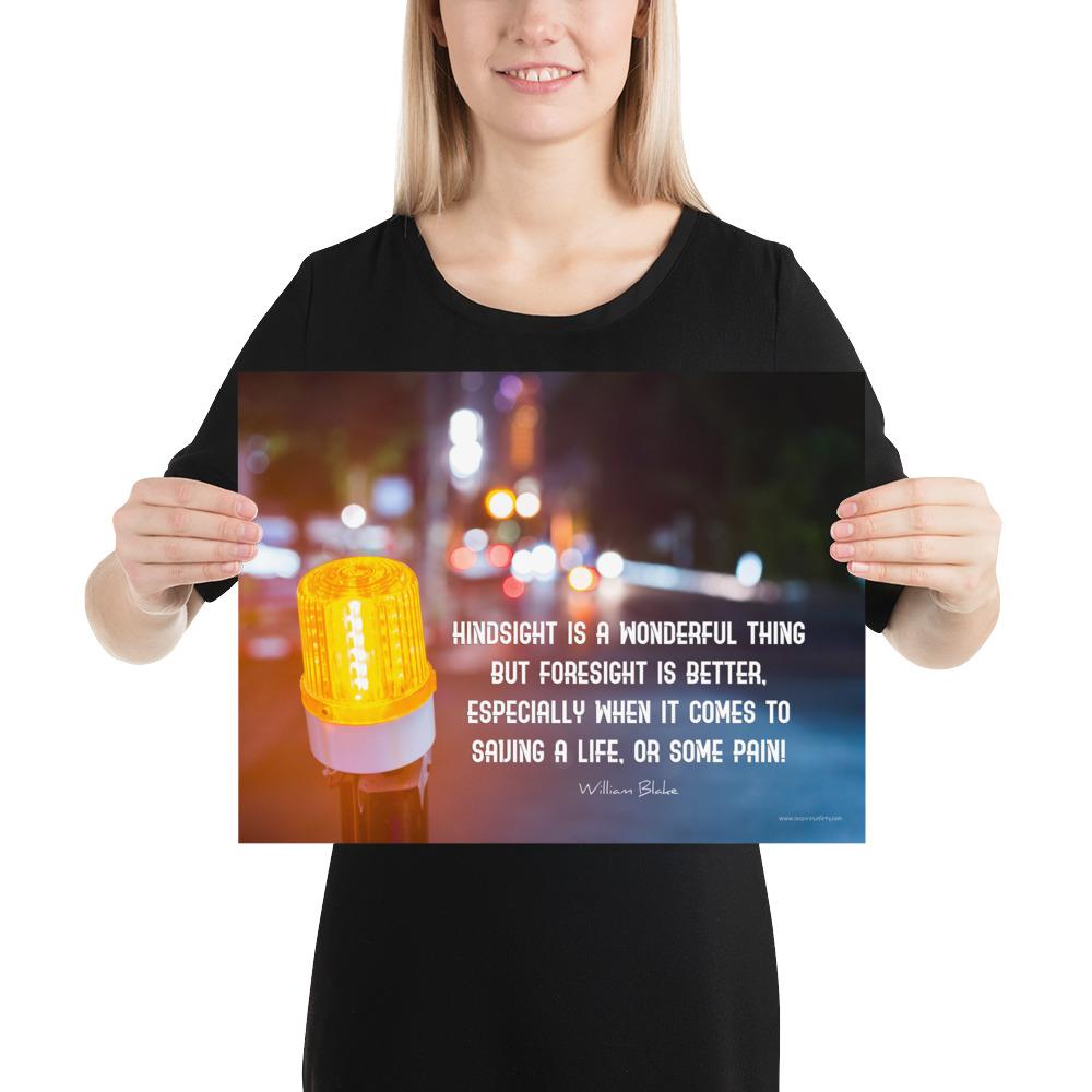 A workplace safety poster depicting a bright orange construction traffic light in the foreground of a blurry nighttime cityscape with a safety quote by William Blake.