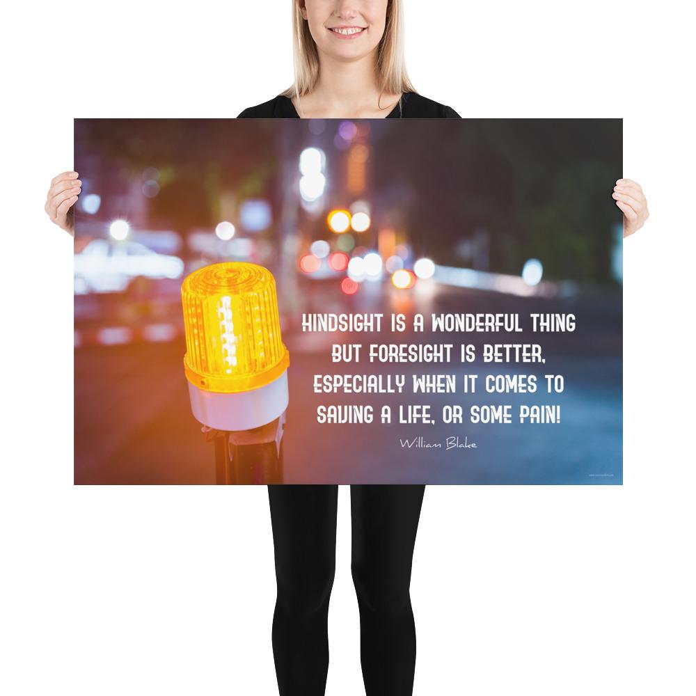 A workplace safety poster depicting a bright orange construction traffic light in the foreground of a blurry nighttime cityscape with a safety quote by William Blake.