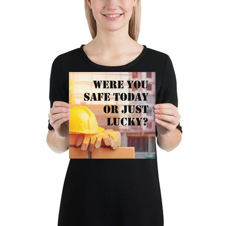 A workplace safety poster showing a yellow hard hat and some gloves sitting on a brick wall on a construction site with the slogan were you safe today, or just lucky written in black stencil font.