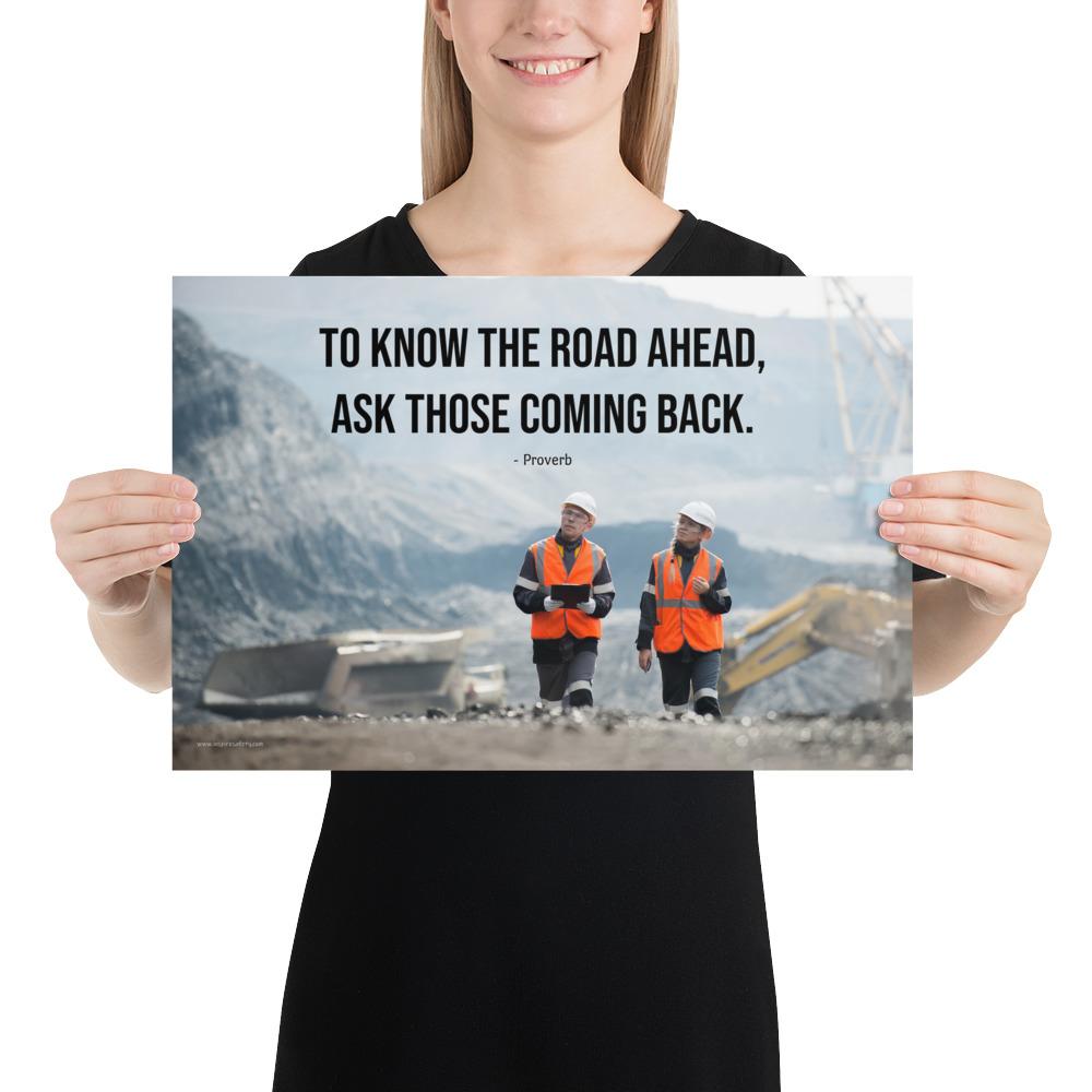 A safety poster showing two workers in reflective vests collaborating on a construction site with the proverb to know the road ahead ask those coming back.