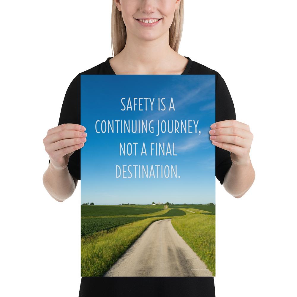 A workplace safety poster depicting a beautiful sunny day with a bright blue sky and a lush green field being cut down the middle by a dirt road leading off into the countryside with the text safety is a continuing journey, not a final destination.