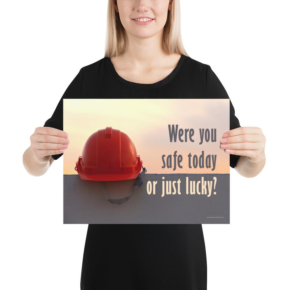 A workplace safety poster showing a red hard hat sitting on a grey wall with a dreamy sunset background and the slogan were you safe today, or just lucky?