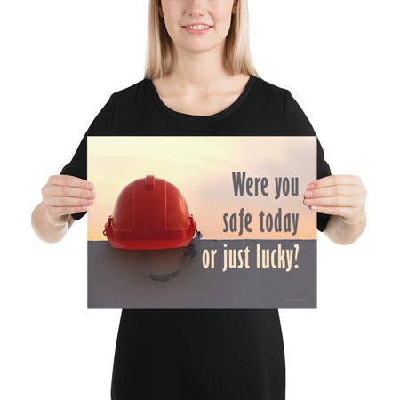 A workplace safety poster showing a red hard hat sitting on a grey wall with a dreamy sunset background and the slogan were you safe today, or just lucky?