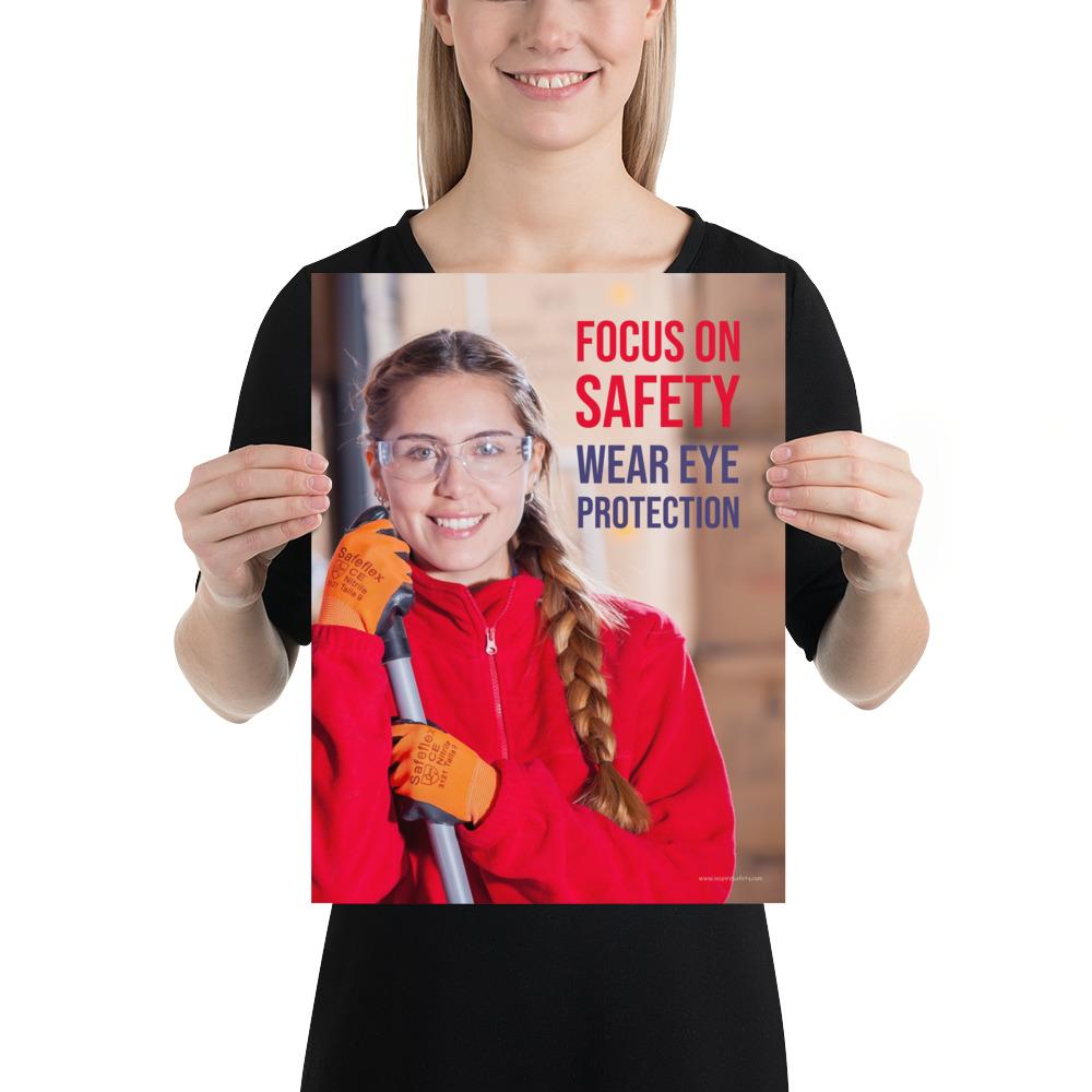 An eye safety poster of a young woman wearing safety glasses and orange gloves smiling as she works in a warehouse with a safety slogan in the top right corner.