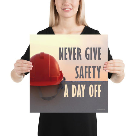 A workplace safety poster depicting a red hard hat sitting on a concrete wall with a dreamy pink sunset in the background with the text never give safety a day off to the right.