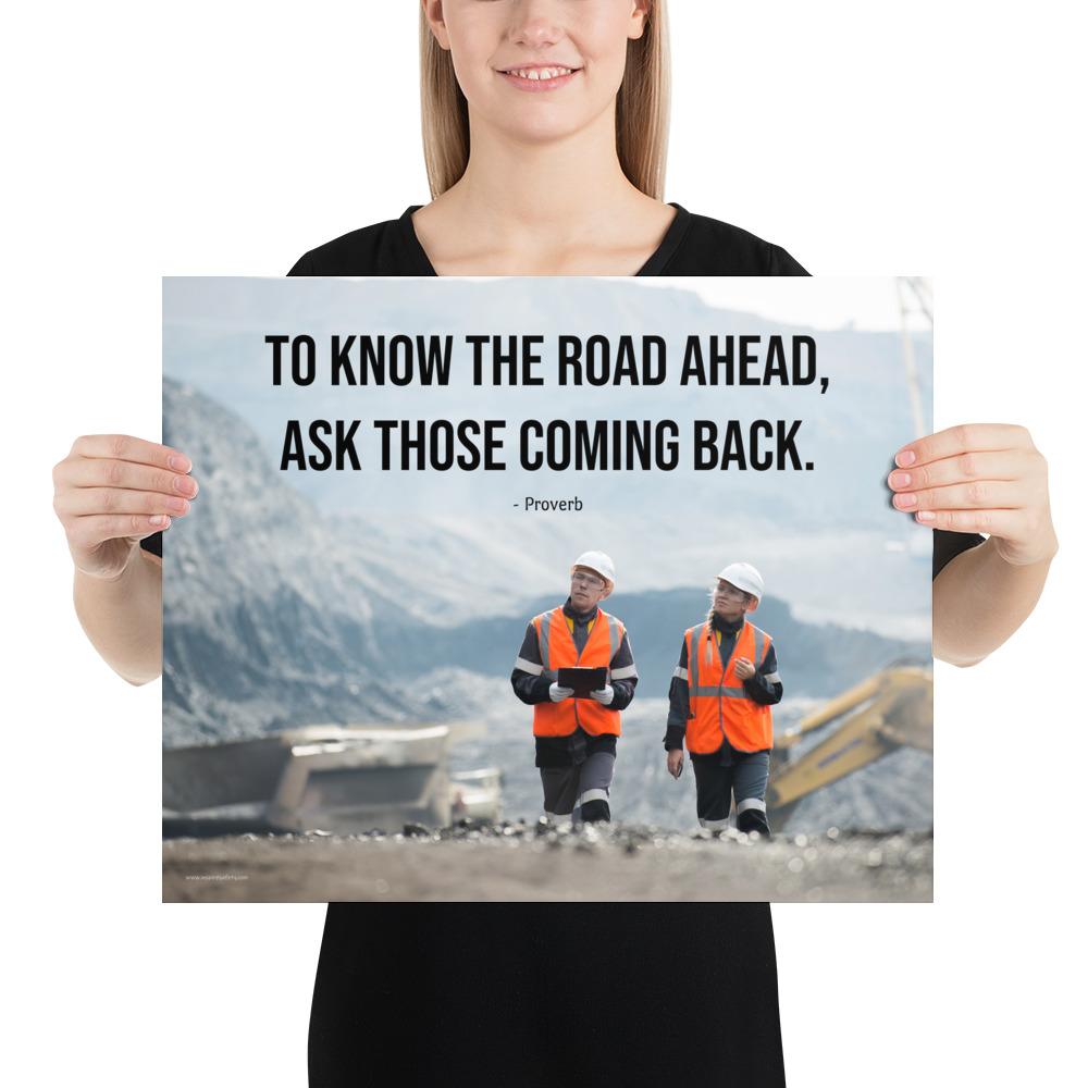 A safety poster showing two workers in reflective vests collaborating on a construction site with the proverb to know the road ahead ask those coming back.