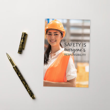 A workplace print showing a young warehouse worker in a yellow hardhat and orange reflective vest holding a clipboard and smiling with the slogan safety is everyone's responsibility.