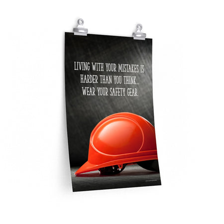 A workplace safety poster showing a bright red hard hat with an ominous black background with the slogan living with your mistakes is harder than you think, wear your safety gear.