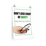 An eye safety slogan showing a close up of a hand presenting out safety glasses with a safety slogan in blue text above.